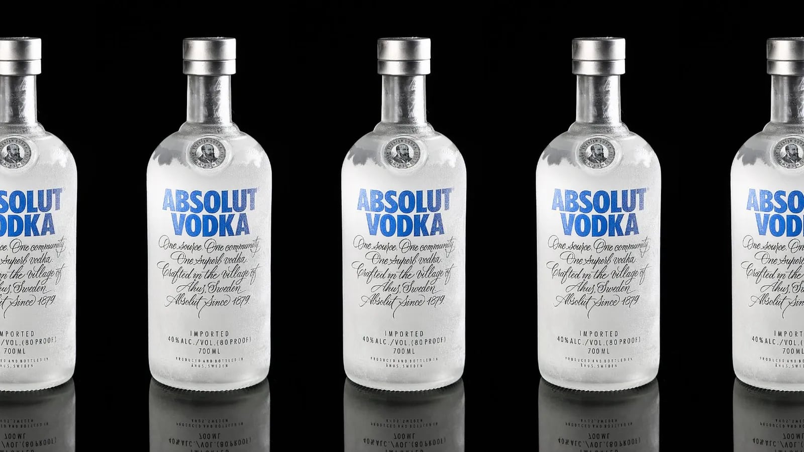 A row of Absolut Vodka bottles on a black background.
