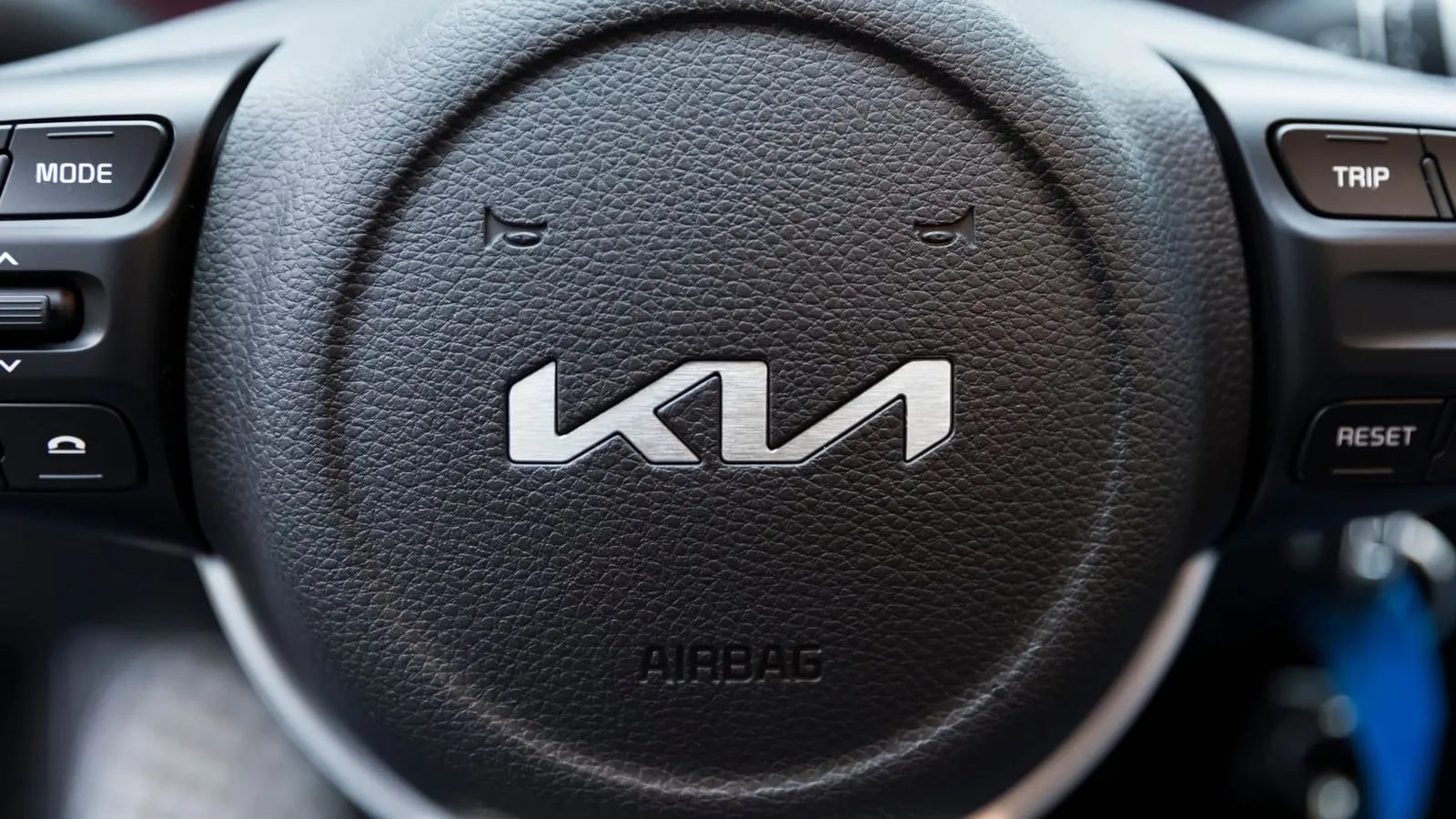 The new Kia logo on a car steering wheel.