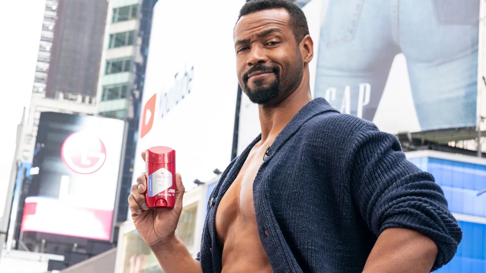 The Old Spice spokesman holding a bottle of Old Spice in a city street ad.