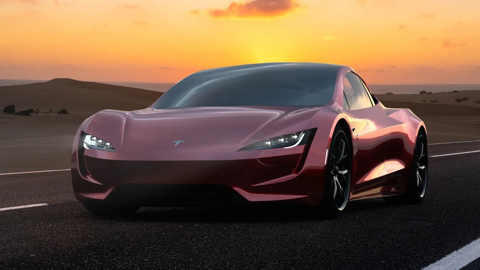 A red Tesla Roadster on a desert road at sunset.