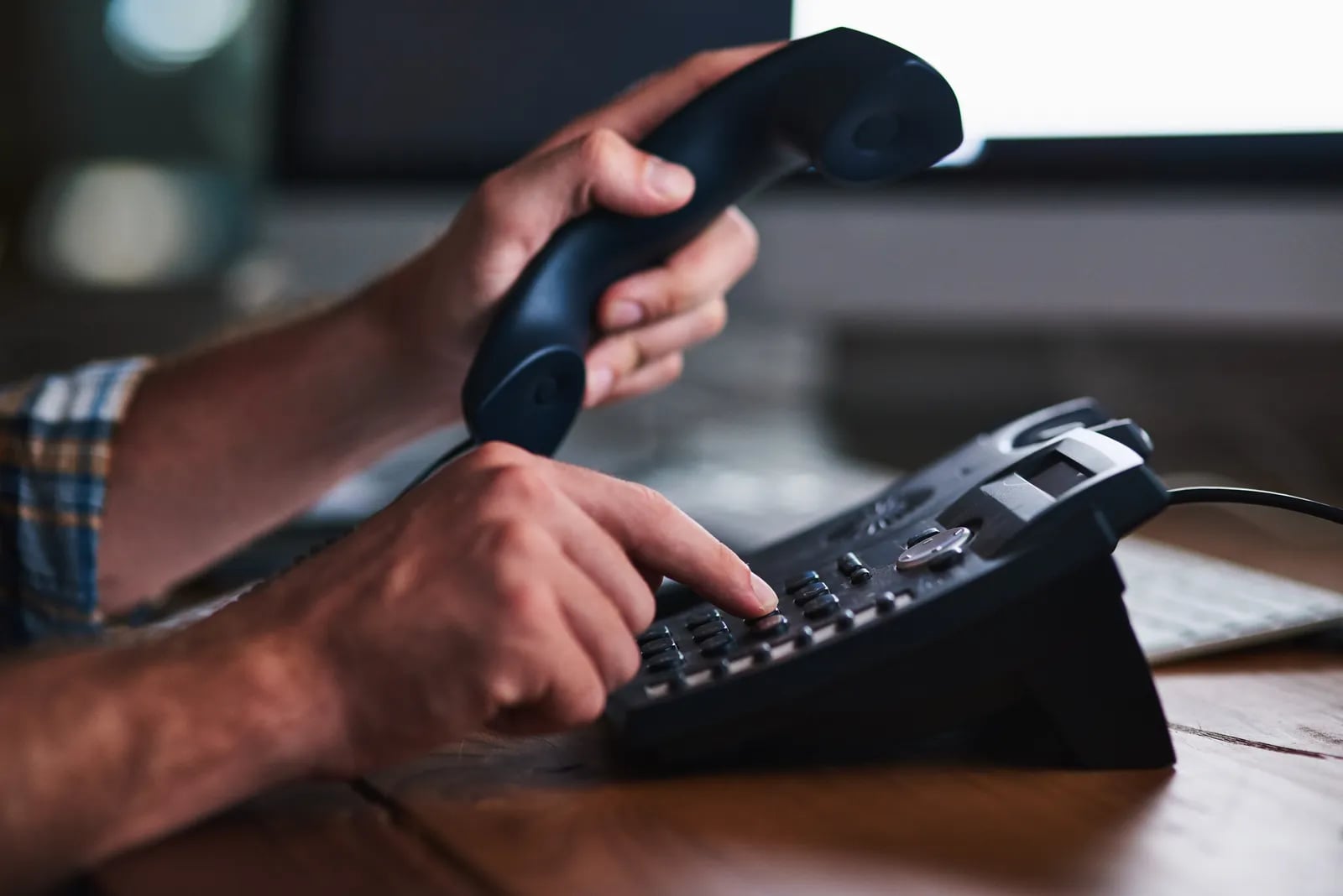 A hand dialling a number on a black desk phone.
